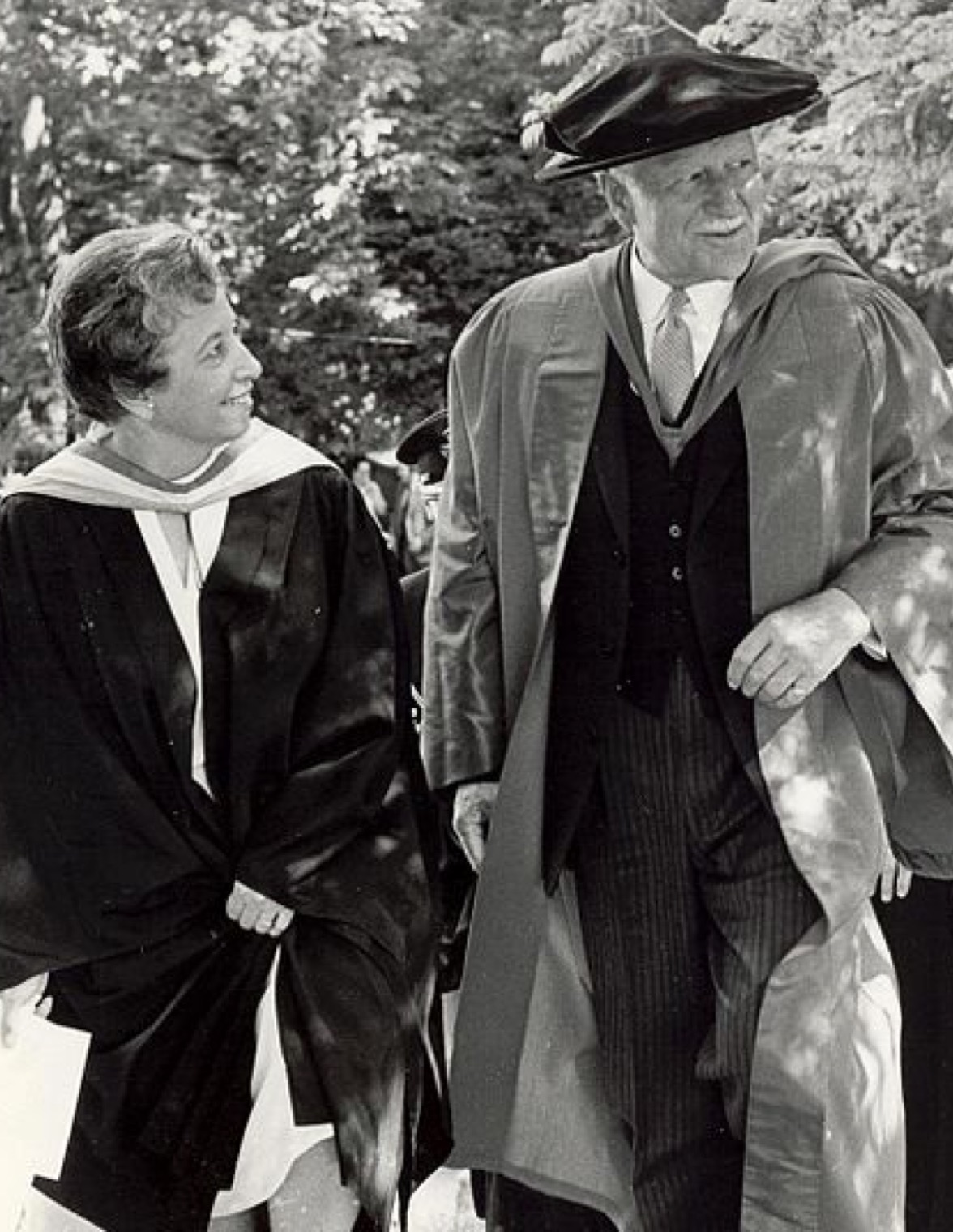 A woman and a man are walking side by side. Both are dressed in academic robes.