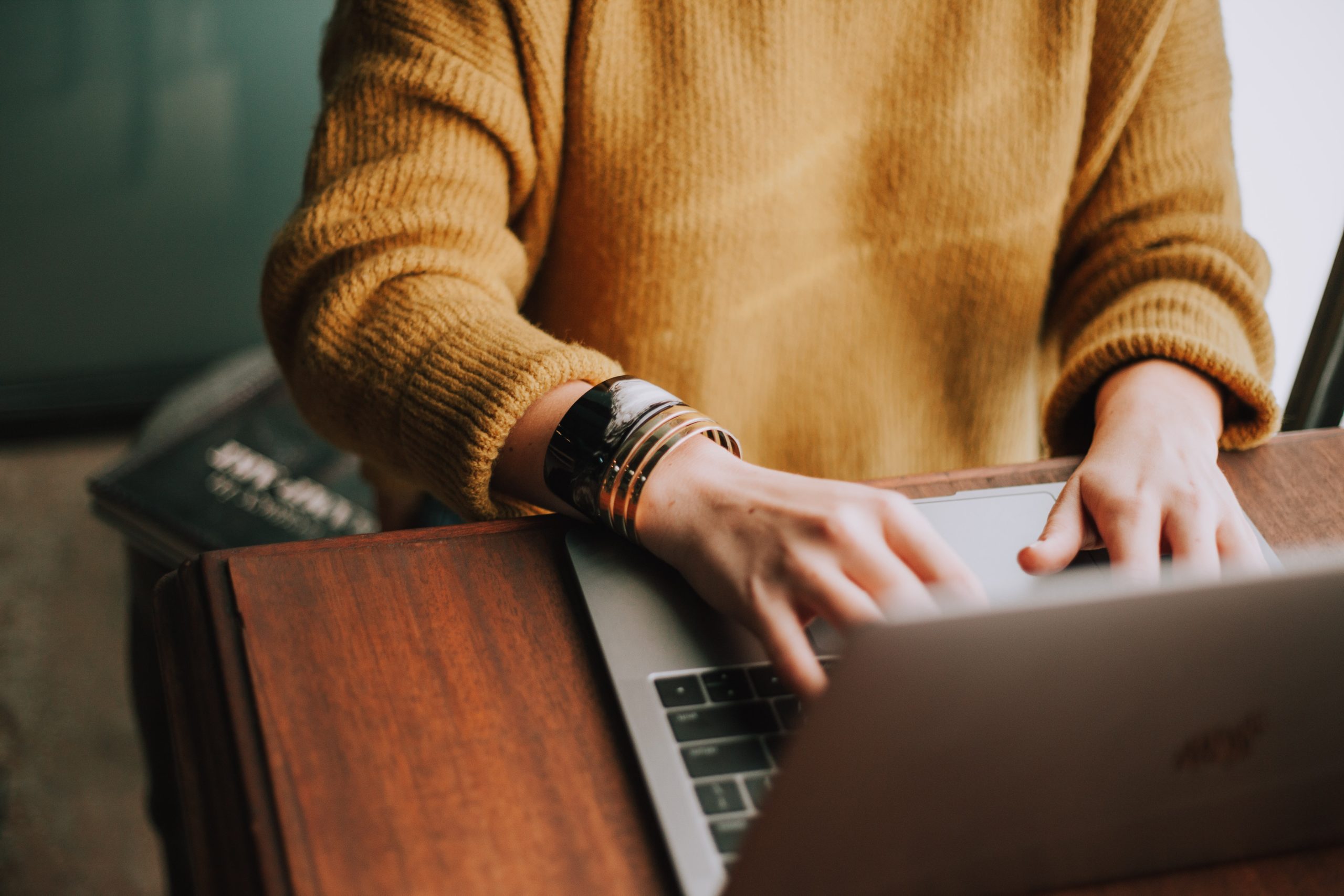 A person in a yellow sweater typing on a laptop.